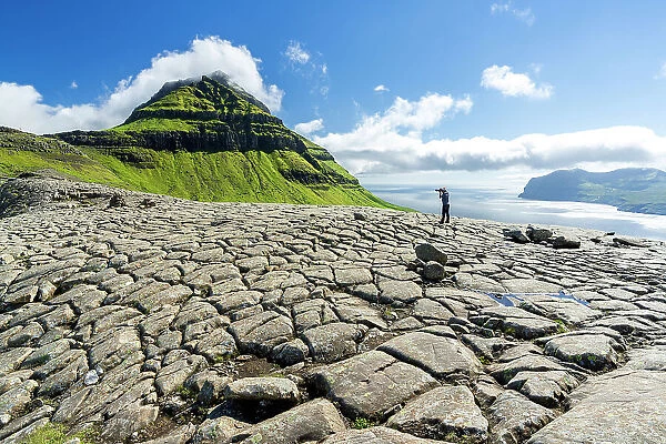 One tourist photographing Skaelingsfjall mountain standing on cracked soil in summer, Streymoy Island, Faroe Islands, Denmark, Europe