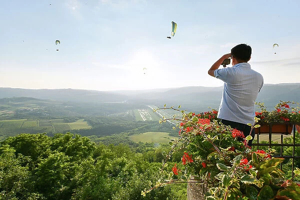 A tourist photographs paragliders from atop the hilltop village of Motovun, Istria, Croatia, Europe