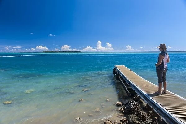 Tourist standing on a little pier with Cocos Island in the distance, Guam, US Territory, Central Pacific, Pacific