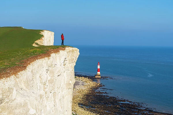 Tourist stands on top of the cliff overlooking Beachy Head lighthouse, Seven Sisters chalk cliffs, South Downs National Park, East Sussex, England, United Kingdom, Europe