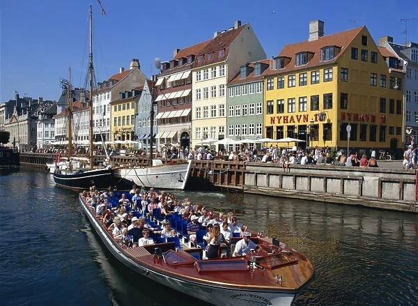 Tourists on boat trip pass painted buildings on the busy waterfront of Nyhavn