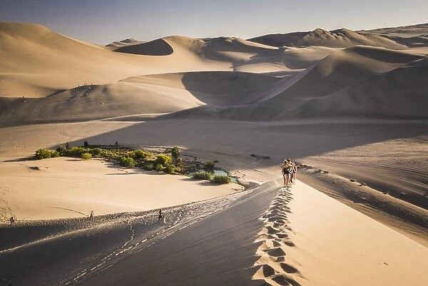 Tourists climbing sand dunes at sunset at Huacachina, a village in the desert, Ica Region