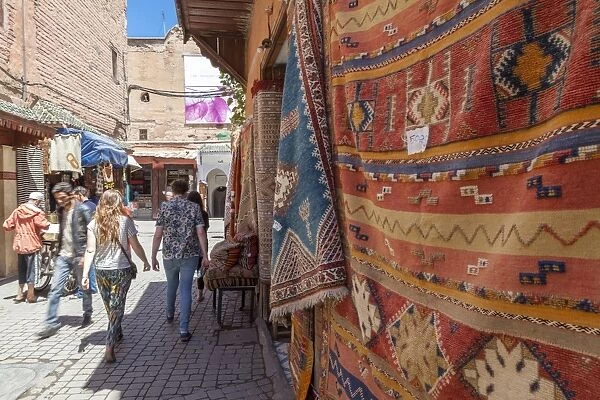 Tourists and locals walking alongside traditional rugs in the Medinas souks, Marrakech, Morocco, North Africa, Africa