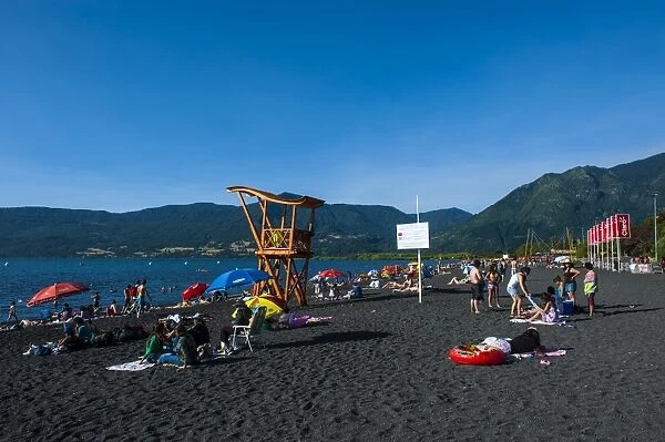 Tourists sunbathing on the volcanic sand beach on Lago Villarrica, Pucon, Chile, South America