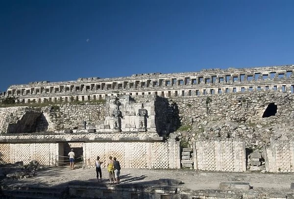 Tourists in front of the unusual restored Atlantes stone carved male figures at rear of the Palace of Masks, Kabah, Yucatan, Mexico