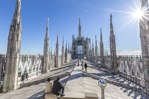 Tourists among the white marble spiers on the top of the Duomo, Milan, Lombardy, Italy