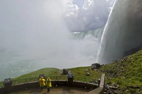 Two tourists in yellow raincoats in the spray of the Horseshoe Falls waterfall whilst on the Journey under the Falls tour at Niagara Falls, Ontario, Canada