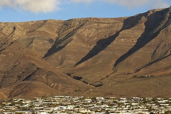 Towering volcanic cliffs of the Risco de Famara rising over low-rise bungalow development near Lanzarotes finest surf beach at Famara, Lanzarote, Canary Islands, Spain, Atlantic