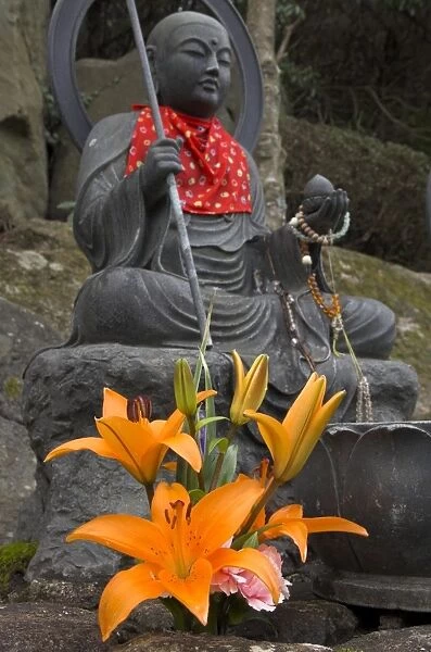 Traditional bronze figure of Buddha with red scarf and fresh flowers