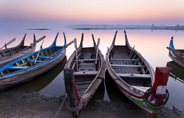 Traditional rowing boat moored on the edge of flat calm Taungthaman Lake at dawn with the colours of the sky reflecting in the calm water, close to the famous U Bein teak bridge, near Mandalay, Myanmar (Burma), Asia