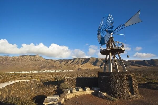 Traditional wind pump with 600m volcanic cliffs of the Risco de Famara rising over desert landscape near Famara in the north west of the island, Famara, Lanzarote, Canary Islands, Spain, Atlantic
