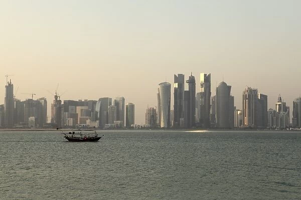 A traditional wooden dhow boat sails past modern skyscrapers in the West Bay financial district of Doha, Qatar, Middle East
