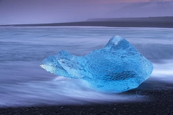 Translucent blue iceberg washed ashore on Breidamerkursandur black sands