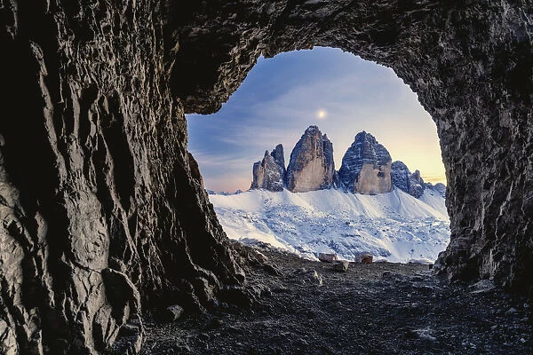Tre Cime di Lavaredo lit by moon seen from opening in rocks of a war cave