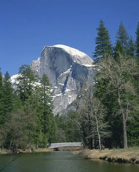 Trees beside a river frame the snow capped Half Dome