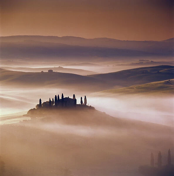 Tuscan farmhouse with cypress trees in misty landscape at sunrise