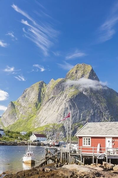 Typical house of fishermen called Rorbu framed by rocky peaks and blue sea, Reine