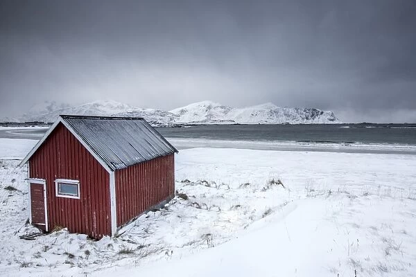 A typical house of the fishermen called rorbu on the snowy beach frames the icy sea at Ramberg