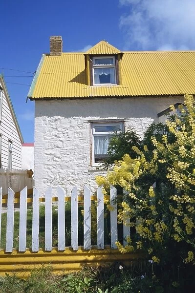 Typical house, with yellow corrugated roof and white stone walls and fence