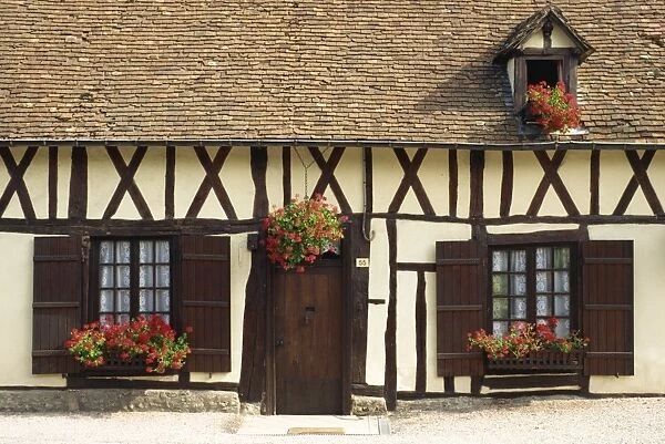 Typical timbered French cottage with geraniums in window boxes and hanging basket