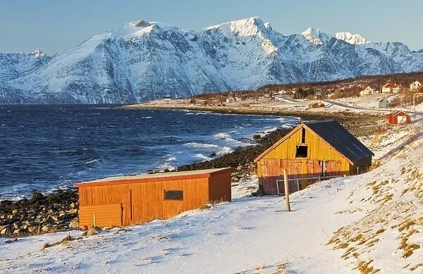 Typical wooden huts called Rorbu surrounded by waves of the cold sea and snowy peaks