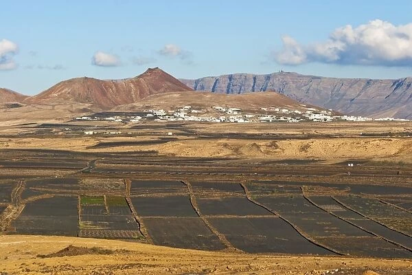 View across black volcanic cinder fields to the town of Soo and the Risco de Famara range with the highest point on the island at Penas del Cache radar site, Soo, Lanzarote, Canary Islands, Spain, Atlantic