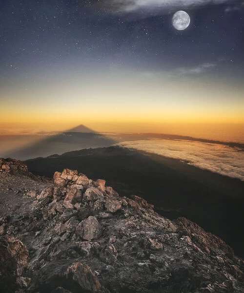 View of El Teide volcano shadow and full moon from the summit right before the sunrise
