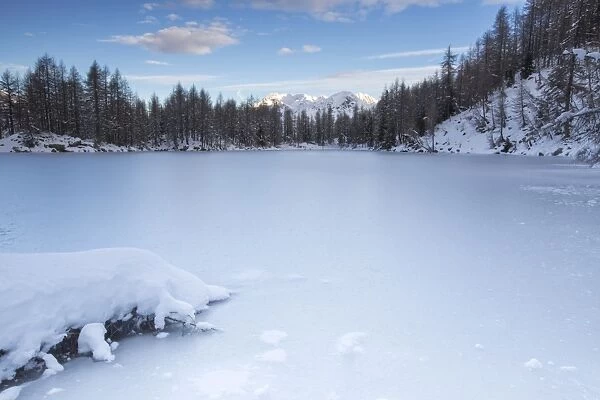 View of the frozen Lago Azzurro surrounded by snow at dawn, Spluga Valley, Province of Sondrio