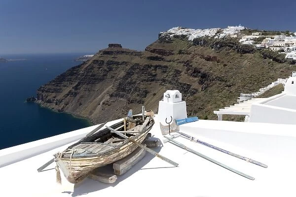 View towards Imerovigli from Firostefani with old rowing boat on hotel roof, Santorini