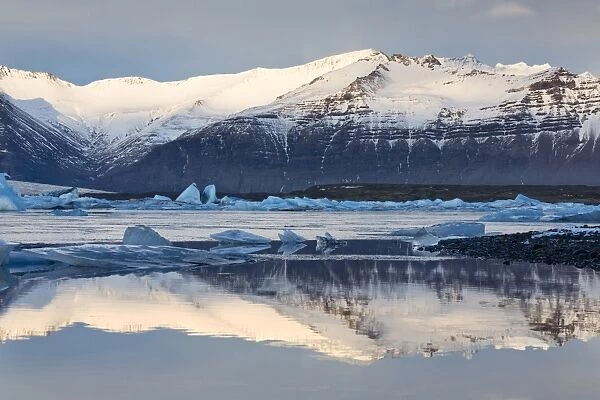 View over Jokulsarlon glacial lagoon towards snow-capped mountains and icebergs, with reflections in the calm water of the lagoon, at the head of the Breidamerkurjokull Glacier on the edge of the Vatnajokull National Park, South Iceland, Iceland, Polar Regions