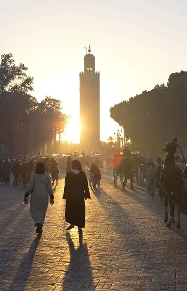 View towards the Koutoubia Minaret at sunset with local people walking through the scene, Djemaa el Fna, Marrakech, Morocco, North Africa, Africa
