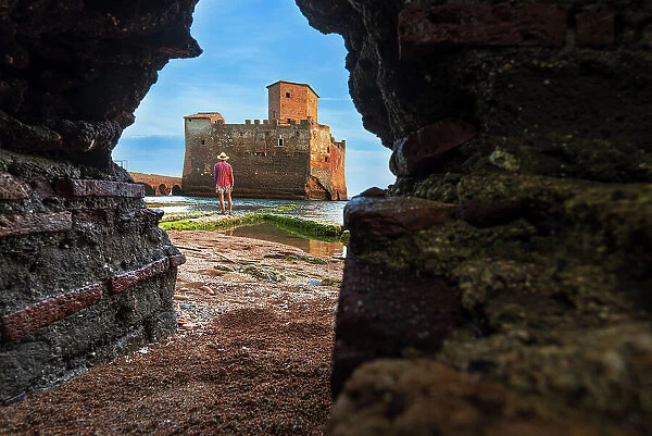 View from below of a man standing in front of the castle of Torre Astura seen through a hole in the wall, Rome province, Tyrrhenian sea, Latium (Lazio), Italy, Europe