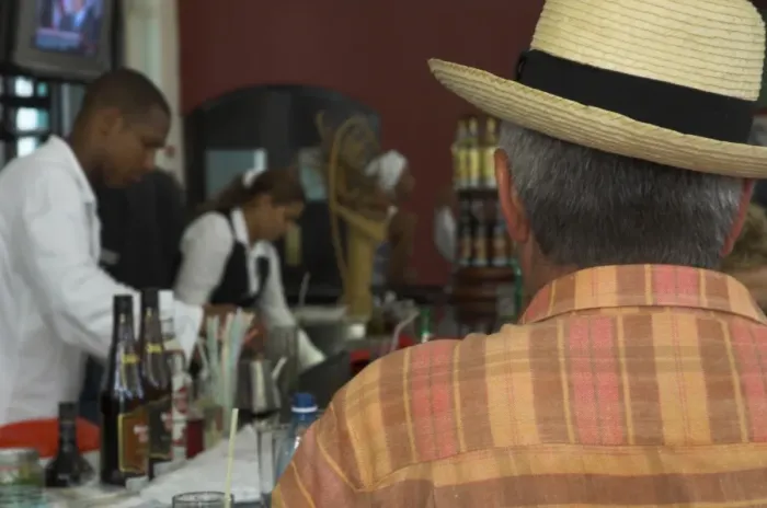 Framed Print : Back view of a man in a straw hat sitting at a bar, with bar staff in the background Framed Print : Back view of a man in a straw hat sitting at a bar, with bar staff in the background
