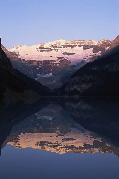 View to Mount Victoria across the still waters of Lake Louise, at sunrise in summer