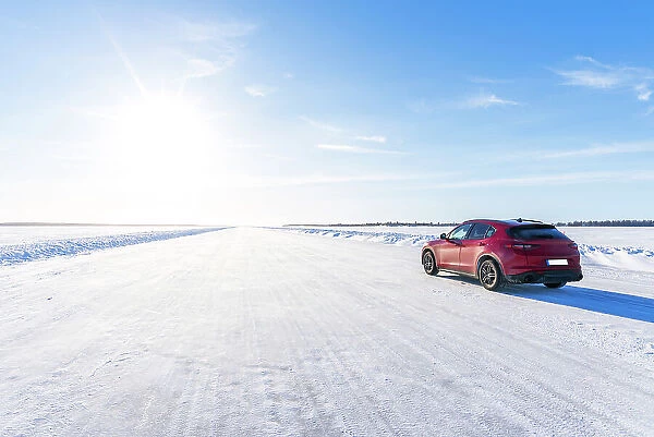 Side view of a red car travelling on empty icy road on the frozen sea, Lulea, Norrbotten County, Lapland, Sweden, Scandinavia, Eurupe