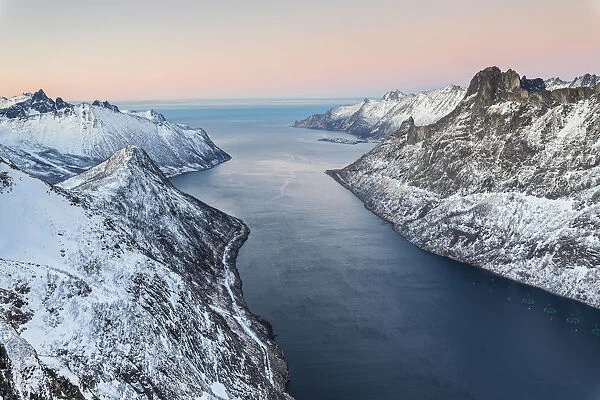Top view of the snowy peaks surrounding Fjordgard framed by the frozen sea at sunset