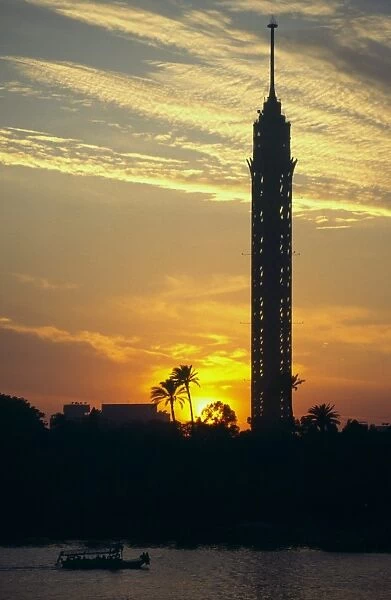 View at sunset of the Tower of Cairo and palm trees with small boat on River Nile in foreground
