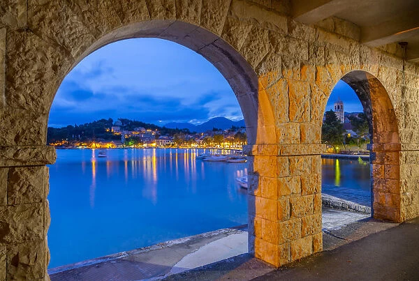 View of town and Crkva Sv. Nikole church through arches at dusk, Cavtat on the Adriatic