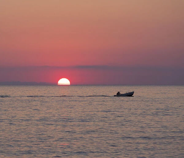 View across the Tyrrhenian Sea at sunrise, small boat crossing Calura Bay, Cefalu