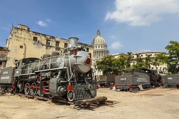 A vintage steam train in a restoration yard with the dome of the former Parliament
