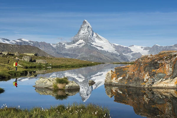 A walker hiking in the Alps takes in the view of the Matterhorn reflected in Stellisee