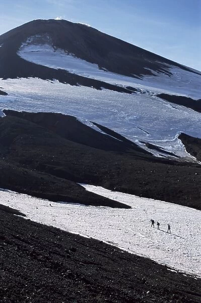 Walkers on snow field below steaming summit cone