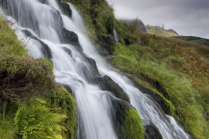 Framed Print : Waterfall cascading down grassy slope with Old Man of Storr in background Framed Print : Waterfall cascading down grassy slope with Old Man of Storr in background