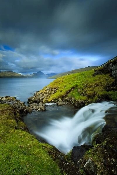 A waterfall cascading into the Vestmannasund, in the background is the picturesque island of Streymoy, Oyrargjogv, Vagar Island, Faroe Islands