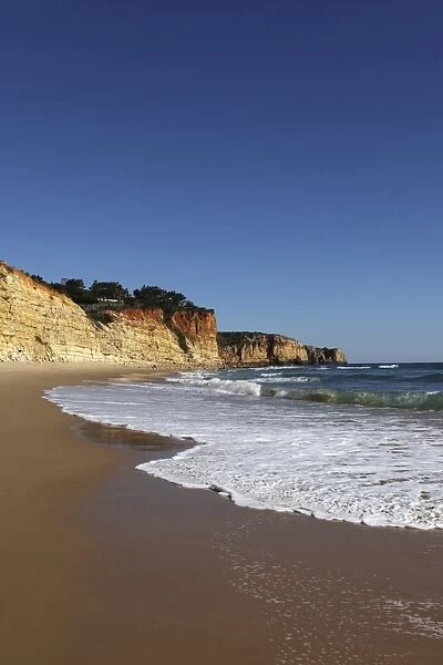 A wave breaks on golden sands flanked by steep cliffs, typical of the Atlantic coastline near Lagos, Algarve, Portugal, Europe