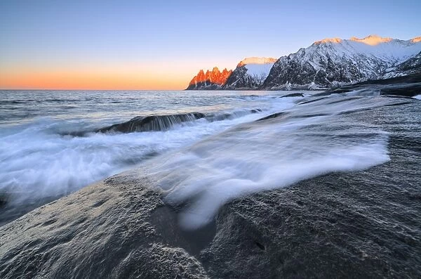 The waves of the icy sea crashing on the rocky cliffs at dawn Tungeneset, Senja, Troms county