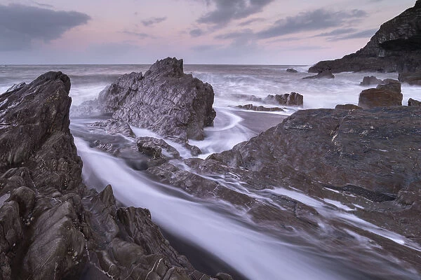 Waves surge around the jagged rocks on Wildersmouth Beach, Ilfracombe, Devon, England