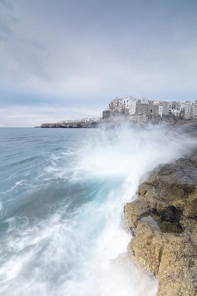 Waves of turquoise sea crashing on cliffs framed by the old town, Polignano a Mare
