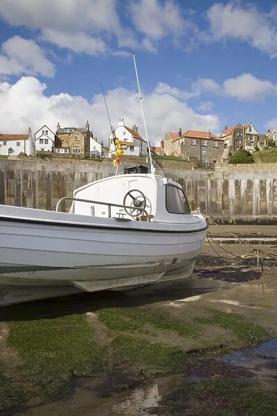 White boat on The Landing in harbour at low tide with Old Bay area of fishing village above coastal defence sea wall behind, Robin Hoods Bay, Yorkshire, England, United