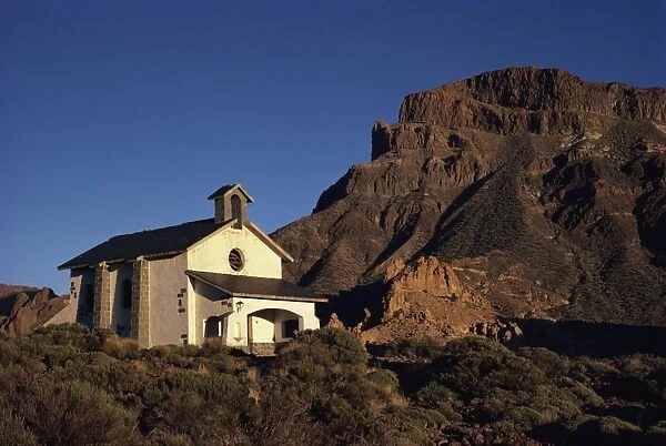 White church in rough desert below a rocky hill in the Canadas del Teide National Park